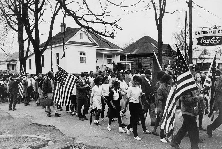 African American civil rights marchers, some carrying American flags, marching from Selma to Montgomery, Alabama, in 1965.